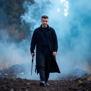 Илья Шведков в длинном чёрном пальто идёт по полю боя после битвы, поднимается дым, лицо без эмоций, энергия современного самурая